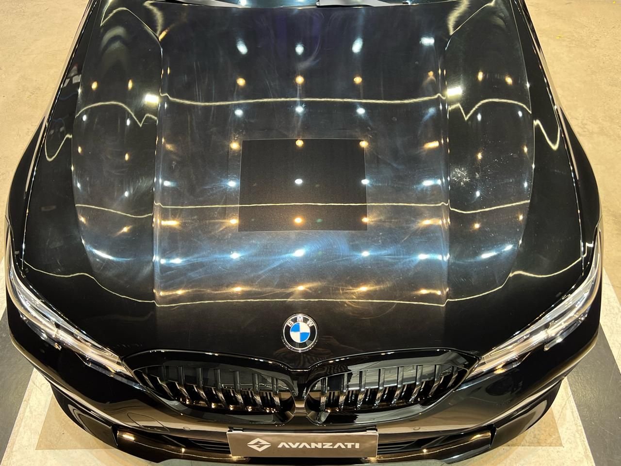 Capô preto de BMW com uma área quadrada de teste já polida, cercada de teias de aranha