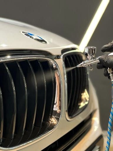 Aerógrafo aplicando produto na grade duplo rim de um BMW branco